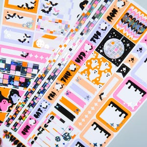 May include: A set of Halloween themed planner stickers with orange, pink, black, and white colors. The stickers feature ghosts, bats, stars, and a disco ball. The stickers also include the days of the week, "Mon", "Tue", "Wed", "Thu", "Fri", "Sat", "Sun".