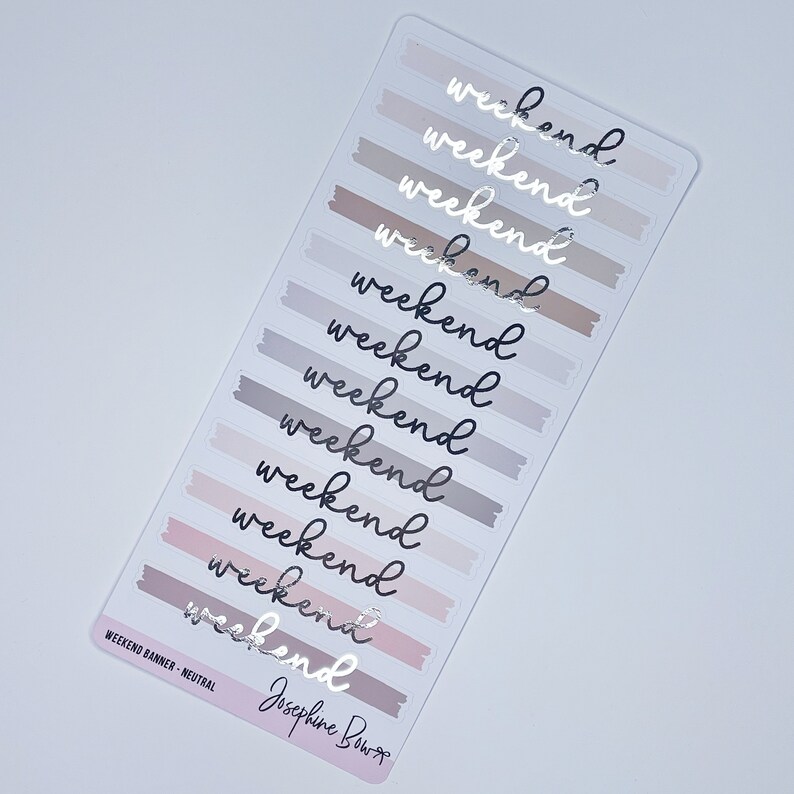 May include: A sheet of neutral-toned weekend planner stickers. Each sticker features the word "weekend" in a handwritten font, with a brushstroke banner in shades of gray, taupe, and pink. The text "WEEKEND BANNER - NEUTRAL" and a signature are at the bottom.
