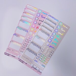 Puede incluir: Dos juegos de pegatinas para planificadores con acabado holográfico. Las pegatinas están sobre un fondo rosa y beige. Las pegatinas presentan una variedad de formas y tamaños, incluyendo círculos, cuadrados y rectángulos. Las pegatinas están decoradas con una variedad de patrones, incluyendo lunares, rayas y corazones. Las pegatinas están etiquetadas como "SV ONE PO MINI KIT - STRAWBERRY" y "SV ONE PO MINI KIT - SAND".
