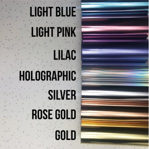 May include: A close-up of seven different colored rolls of vinyl adhesive. The colors are light blue, light pink, lilac, holographic, silver, rose gold, and gold.