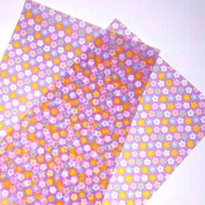 Può includere: Tre fogli di carta fantasia con un motivo floreale. La carta ha uno sfondo lilla con piccoli fiori gialli, bianchi, blu e arancioni. I fogli si sovrappongono, creando un effetto a strati.