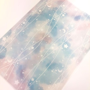 Può includere: Un foglio rettangolare con un design ad acquerello con un cielo sognante di tonalità blu, rosa e viola. Stelle bianche, lune e linee curve sovrappongono lo sfondo, creando un motivo celeste. L'estetica generale è morbida ed eterea.