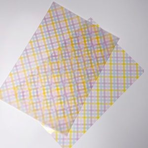 Può includere: Vista dall'alto di tre fogli di carta traslucida con un motivo a quadri pastello. Il motivo a quadri presenta linee che si intersecano in giallo, blu e viola. I fogli sono disposti ad angolo su uno sfondo bianco.