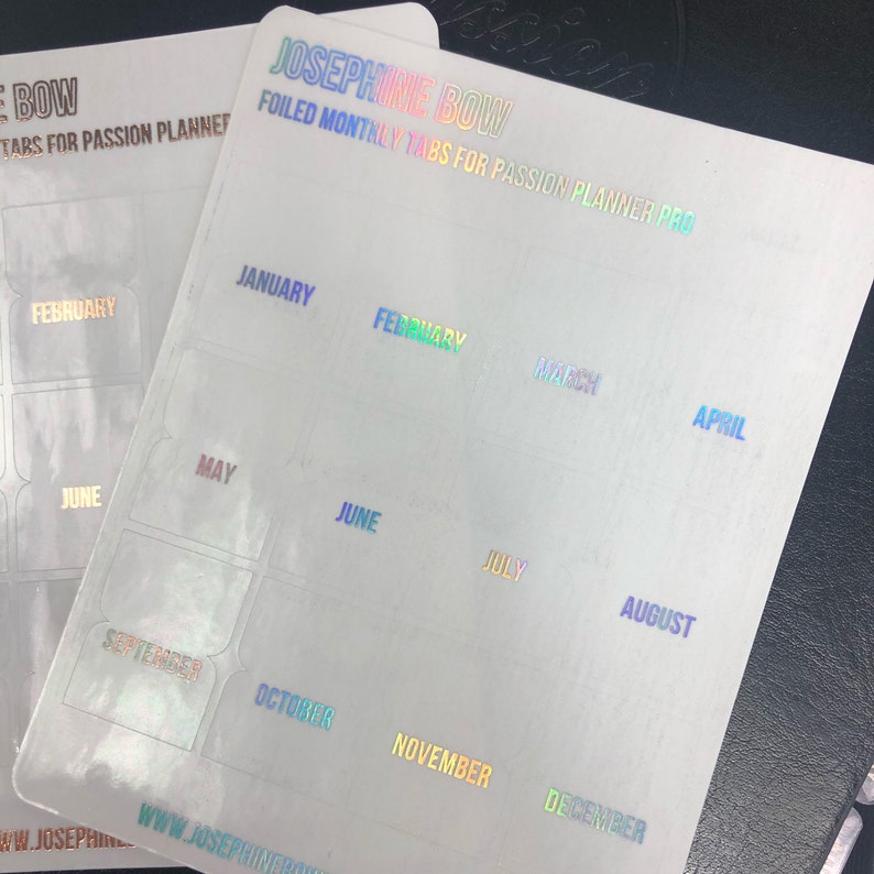 May include: A set of 12 iridescent holographic monthly planner tabs with the months of the year printed in rainbow colors. The tabs are labeled January through December. The tabs are designed for the Passion Planner Pro.