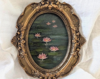 May include: An oval oil painting of pink water lilies on a dark green pond, encased in an ornate, antique-style gold frame with intricate floral and leaf carvings. The painting features visible brushstrokes and the initials LK in the corner.