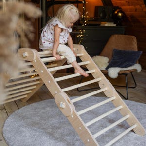 May include: A wooden climbing frame with a ladder and a slide. A young child is climbing up the ladder. The frame is made of natural wood and has a light brown finish.
