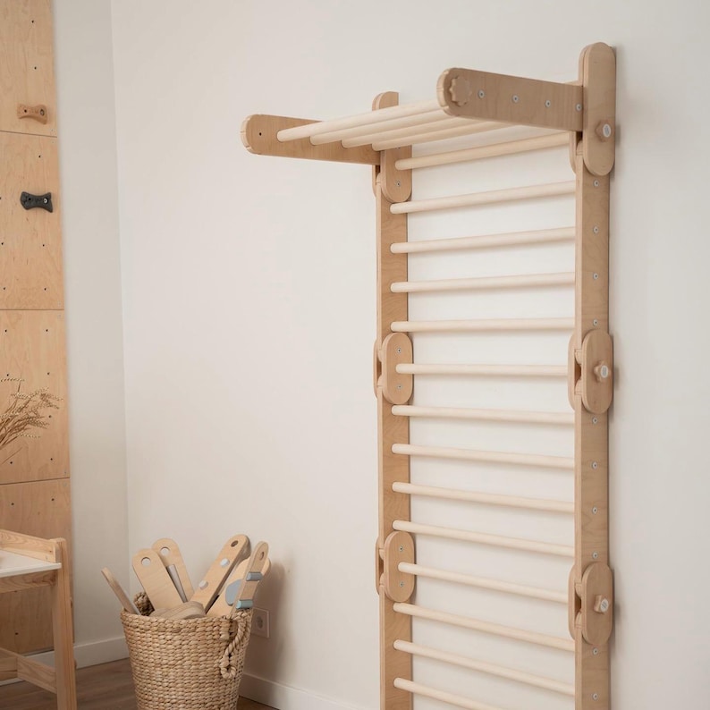 May include: A wooden climbing wall with a ladder and a horizontal bar at the top. The wall is made of light wood and has a natural finish. The ladder has 12 rungs and is attached to the wall with metal brackets. The horizontal bar is also attached to the wall with metal brackets.