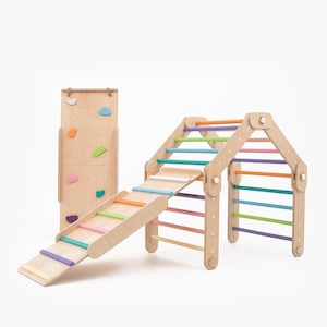 Peut inclure: Structure d'escalade en bois avec un toboggan, un mur d'escalade et des barreaux colorés. La structure est en bois naturel et a une finition brun clair. Le toboggan est en bois et a une finition rose clair. Le mur d'escalade est en bois et a une finition brun clair. Les barreaux sont en bois et sont peints dans une variété de couleurs, y compris le rose, le bleu, le vert et l'orange.