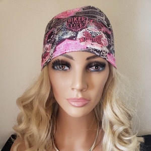 May include: A pink and black bandana with a motorcycle theme. The bandana has the words "Biker for Life" and "Harley Davidson" printed on it. The bandana is worn by a mannequin with blonde hair and a silver necklace with a Harley Davidson logo pendant.