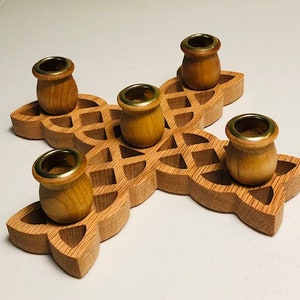 May include: A wooden candle holder with a Celtic knot design and five brass candle cups. The holder is made of light brown wood and has a natural finish.