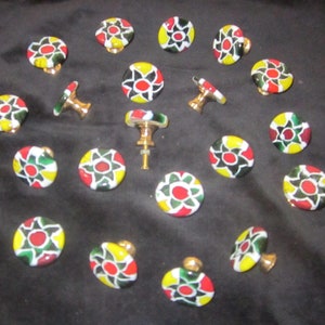 May include: A collection of colorful cabinet knobs with a floral design. The knobs feature a gold base and a circular top with red, yellow, green, and black accents. The knobs are arranged on a black surface.