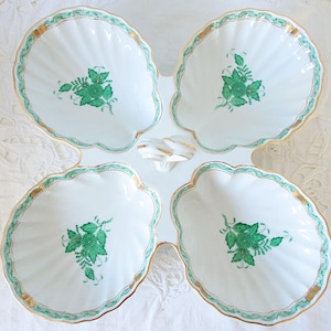 May include: A white porcelain serving dish with four scalloped sections. Each section features a green floral design and gold trim. The dish has a central handle and is suitable for serving snacks or appetizers.