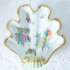 May include: White, shell-shaped decorative dish with a scalloped gold rim. The dish features colorful floral and butterfly designs in pink, blue, orange, and green. The base of the dish is a pale green color.
