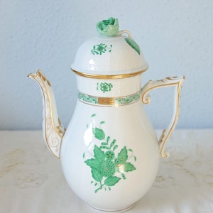 May include: White porcelain coffee pot with green floral design and gold trim. The lid is topped with a green rose. The handle and spout are also trimmed in gold. A decorative piece for the kitchen or dining room.