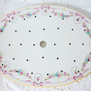 Può includere: Vassoio ovale bianco con un design floreale e a nastro. Il vassoio ha un bordo giallo ed è decorato con fiori rosa, blu e viola e nastri rosa. Ci sono punti neri e un foro centrale.