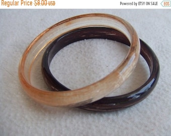 May include: Two plastic bangles, one is a light brown color and the other is a dark brown color.