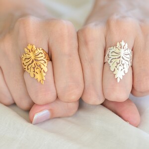 Könnte beinhalten: Zwei Ringe mit einem filigranen, kunstvollen Design, das an einen stilisierten Ast erinnert. Ein Ring ist golden, der andere silbern.