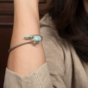 Può includere: Un braccialetto d'argento con una pietra preziosa blu e pietre più piccole che pendono.