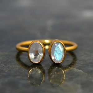 May include: A gold ring with two oval-shaped moonstone gemstones. The ring is open on one side and the stones are set in a bezel setting.