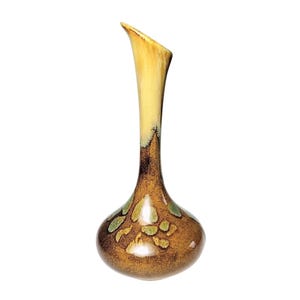 May include: A ceramic vase with a slender, elongated neck and a bulbous base. The upper portion is a smooth, pale cream color, while the lower body features a mottled brown glaze with scattered, irregular green and tan leaf-like shapes.