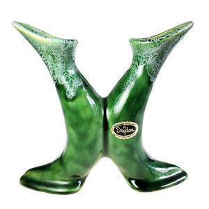May include: A dual-spout ceramic vase with a glossy emerald green glaze and white foam-like texture at the rims. The piece features a central junction and an oval sticker that reads A MILEAGE IN GLAZE BY DRYDEN WITH VOLCANIC ASH.