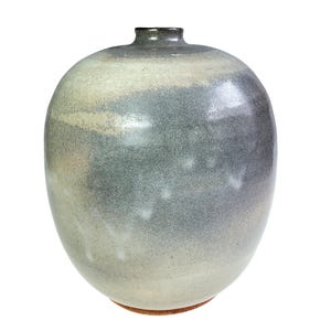 May include: A rounded ceramic vase with a narrow neck and a smooth, glazed finish. The surface features a gradient of colors, transitioning from a light, creamy off-white at the base to a mottled, dusty blue-grey towards the top rim.