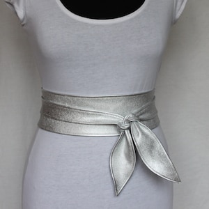 May include: A silver leather belt with a bow knot. The belt is tied around a white shirt.