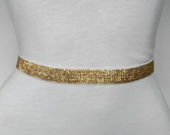 May include: A gold metallic belt with a shimmery finish. The belt is thin and flat, and it is shown against a white background.