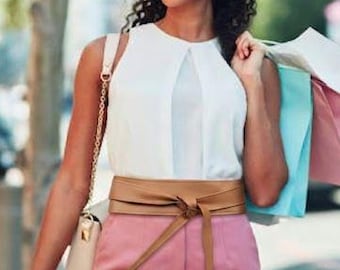 Könnte beinhalten: Ein weißes ärmelloses Oberteil mit Mittelnaht, eine rosa Hose und ein hellbrauner Wickelgürtel mit Bindung in der Taille. Das Outfit umfasst eine cremefarbene Umhängetasche mit goldener Kette und eine große, dunkel getönte Sonnenbrille.