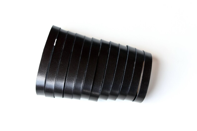 May include: A black leather cuff bracelet with multiple parallel straps. The bracelet is curved and appears to be made of genuine leather. The background is plain white, highlighting the dark color and texture of the leather.