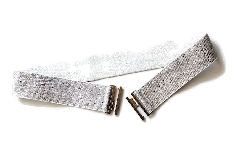 May include: A silver elastic belt with a shiny finish and two gold metal buckles.