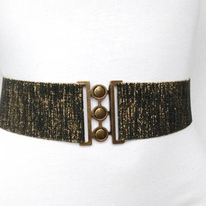 May include: A black and gold elastic belt with a gold metal buckle. The buckle has three round decorative pieces.
