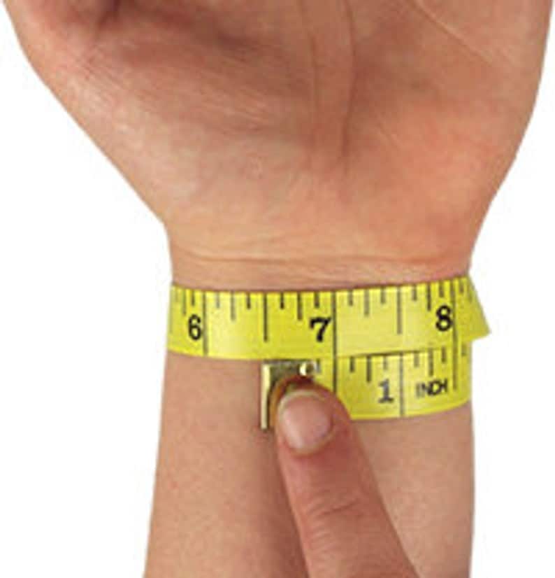 May include: A yellow measuring tape wrapped around a wrist, showing a measurement of approximately 7 inches. The tape is marked with black numbers and inch increments, with the word "INCH" visible.