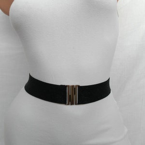 May include: A black elastic belt with a gold metal buckle. The belt is worn over a white vest top.