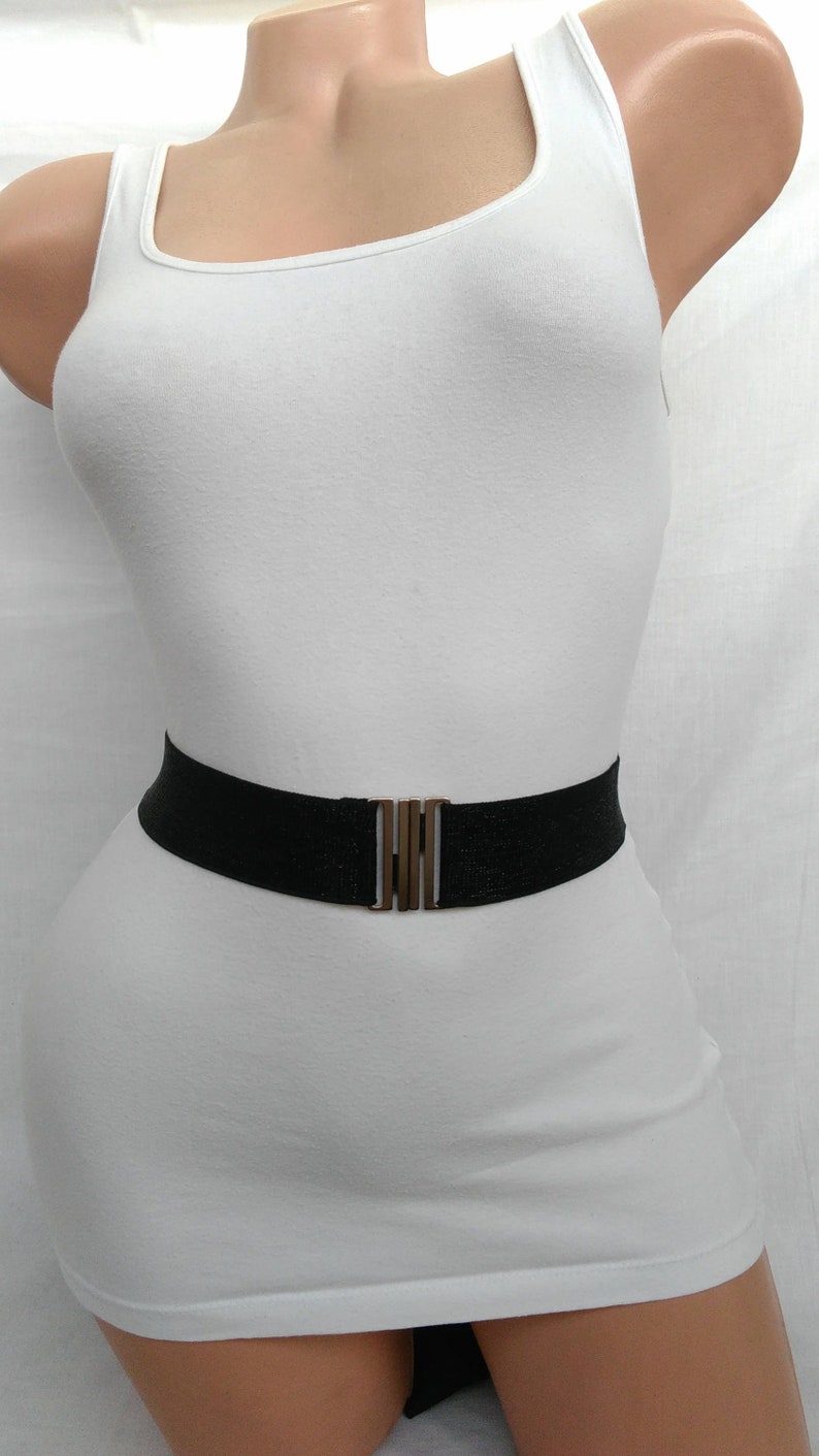 May include: A black elastic belt with a gold metal buckle. The belt is worn over a white vest top.