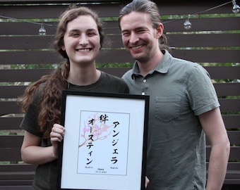 May include: A framed print with a watercolor painting of a cherry blossom branch with pink flowers. The Japanese characters "桜" (sakura), "年" (toshi), "アンジェラ" (Angela), and "オーディン" (Odin) are written in black ink. The text "Shay" and "10-3-2022" are written below the painting.