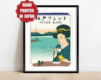 May include: Framed art print featuring a Japanese-style illustration of a woman drinking coffee. The artwork includes the text "MATUDO BLEND" and Japanese characters. The image is set against a teal background with a boat and a tower in the distance. A red badge reads "HAND PAINTED IN JAPAN".