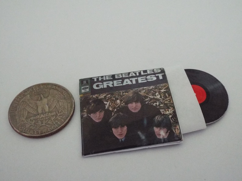 Może przedstawiać: Okładka winylowego albumu z The Beatles z tytułem "The Beatles Greatest" w białym kolorze na czarnym tle. Okładka przedstawia czterech członk&oacute;w zespołu w leśnym otoczeniu.