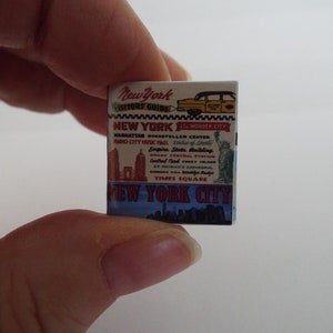 May include: A miniature guide to New York City with a yellow taxi cab on the cover. The guide lists popular attractions like the Empire State Building, Times Square, and Rockefeller Center.