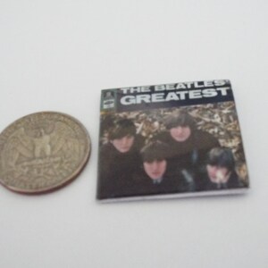 Może przedstawiać: Okładka winylowego albumu z epoki z czarno-białym zdjęciem The Beatles. Tytuł albumu to "The Beatles Greatest" w białym kolorze na czarnym tle.