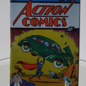 May include: A vintage "Action Comics" comic book cover, dated June 1938, featuring Superman lifting a green car. The cover art shows a dynamic scene with figures in distress and the comic's title in bold red letters.