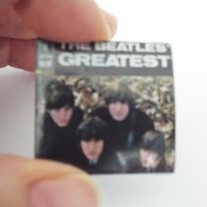 Może przedstawiać: Okładka winylowego albumu z epoki z czarno-białym zdjęciem The Beatles. Tytuł albumu to "The Beatles' Greatest" w białym kolorze na czarnym tle.