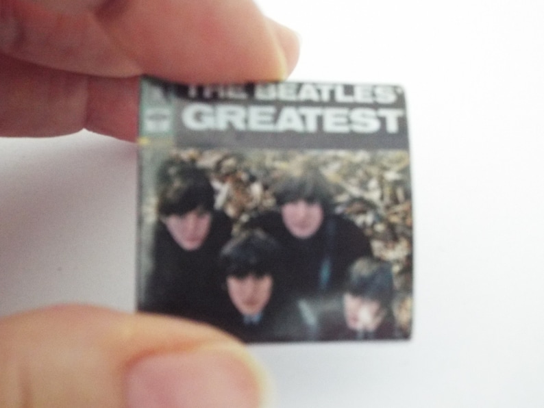 Może przedstawiać: Okładka winylowego albumu z epoki z czarno-białym zdjęciem The Beatles. Tytuł albumu to "The Beatles' Greatest" w białym kolorze na czarnym tle.