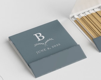 May include: Two matchboxes, one closed and one open, on a white surface. The closed box is teal with the letter "B" and the date "June 8, 2020" printed in white. The open box reveals wooden matches.