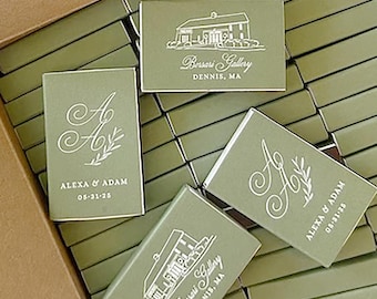 May include: A box filled with olive green matchboxes. Some matchboxes have the text "Alexa & Adam 05-31-25" and a stylized "A" with a floral design. Other matchboxes have the text "Borsari Gallery, Dennis, MA".