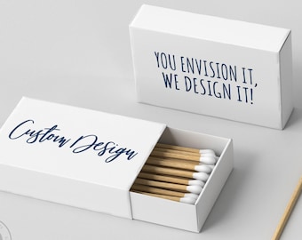 May include: White matchboxes with custom design text in a navy blue script. One box is open, revealing wooden matches with white tips. The text "You Envision It, We Design It!" is on another box.