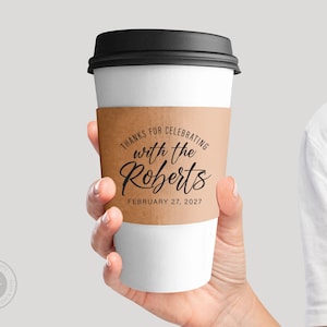Pode incluir: Uma manga de papelão marrom para copo de café com o texto "Obrigado por celebrar com os Roberts em 27 de fevereiro de 2027".