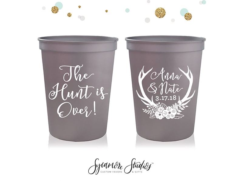 May include: Two gray plastic cups with white text. One cup says "The Hunt is Over!" and the other cup says "Anna & Nate 3.17.18" with a white antler design and floral accents.