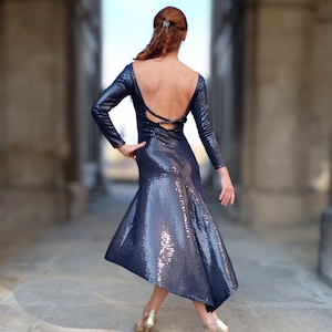 May include: A navy blue sequined dress with long sleeves and an open back. The dress has a flared skirt and is paired with gold high-heeled shoes. The dress is designed for dance or special occasions.