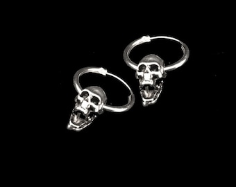 May include: A pair of silver hoop earrings with a skull design. The skulls are facing forward with their mouths open.